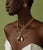 Model on green backdrop wears strapless white top and Mood Necklace in Gold with assorted charms.