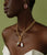 Model on green backdrop wears strapless white top with Tile Earrings in Light Pink and gold necklace with charms.