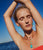 Model against blue sky raises arms up and wears coral top with Cordelia Pendant, Off Shore Necklace and Algarve Earrings