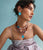 Model on blue backdrop wears floral dress with assorted jewelry including New Bloom Earrings in Cerulean.