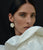 Model on black backdrop wears voluminous white top with New Bloom Earrings in Mother-of-Pearl