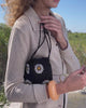 Video of model in beige sweater holding Gala Bag in Midnight Daisy while standing against grassy sand dunes.