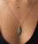 Model's chest in close-up; she wears low-cut black top and silver chain Ceremony Necklace in Dalmatian with jasper pend...