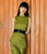 Model on wood panel wall wears green pleated dress, Florence Belt in Black, and Infinity Link Bracelet.