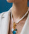 Model on blue background wears cream blazer and the Mood Necklace in Pearl with blue, white, and green charms attached.