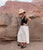 Model standing against desert rocks wears black and white outfit, hat, and Circuit Bangles.