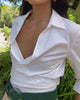Video of model posing against green bushes in white top and cream trousers with Louise Belt in Emerald.