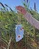 Video of model's hand holding up Gala Bag in Blue Daisy in front of grassy field and blue sky.